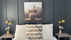 A bedroom with a bed, two bedside tables, a wall-mounted picture, and a nightstand with a lamp.