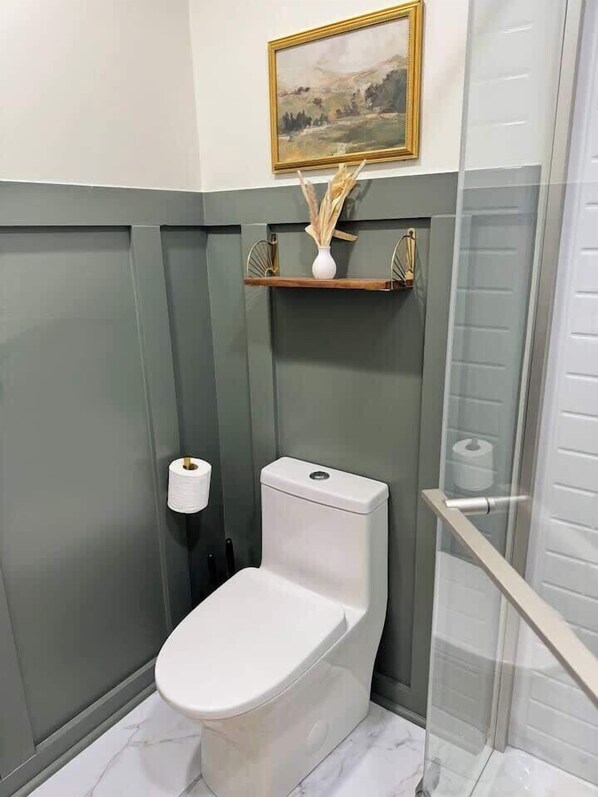 Ein Badezimmer mit Toilette, einer Ablage mit einer Vase und einem gerahmten Bild an der Wand.