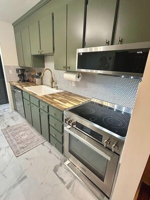 A modern kitchen with green cabinets, a stainless steel stove, and a microwave.