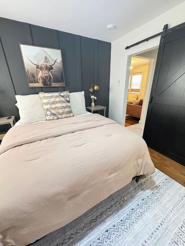 A bedroom with a large bed, a nightstand, a lamp, and a painting on the wall.