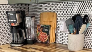 A kitchen with a coffee maker, blender, pizza box, and utensils on the counter.