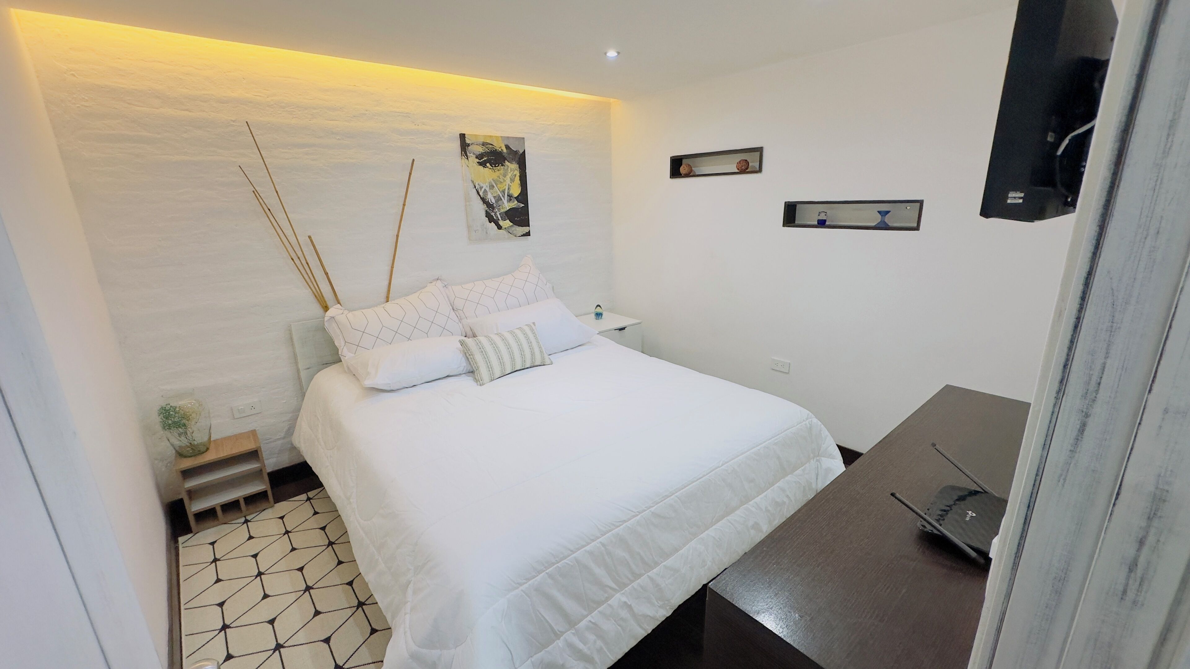 A modern bedroom with a bed, bedside tables, a small plant, and a wall-mounted TV.