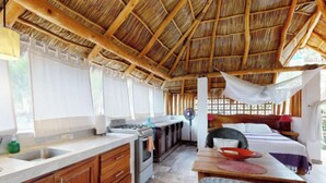 A room with a thatched roof, wooden cabinets, a kitchen area with a stove, and a bed with a canopy. - Aventura Pacifico Boutique Suites Villas (Bucerías)