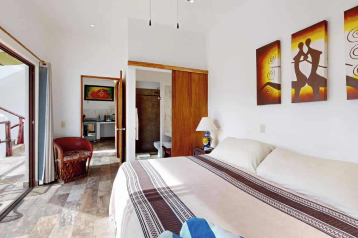 A hotel room with a bed, a chair, a desk, and a bathroom visible through an open door.
