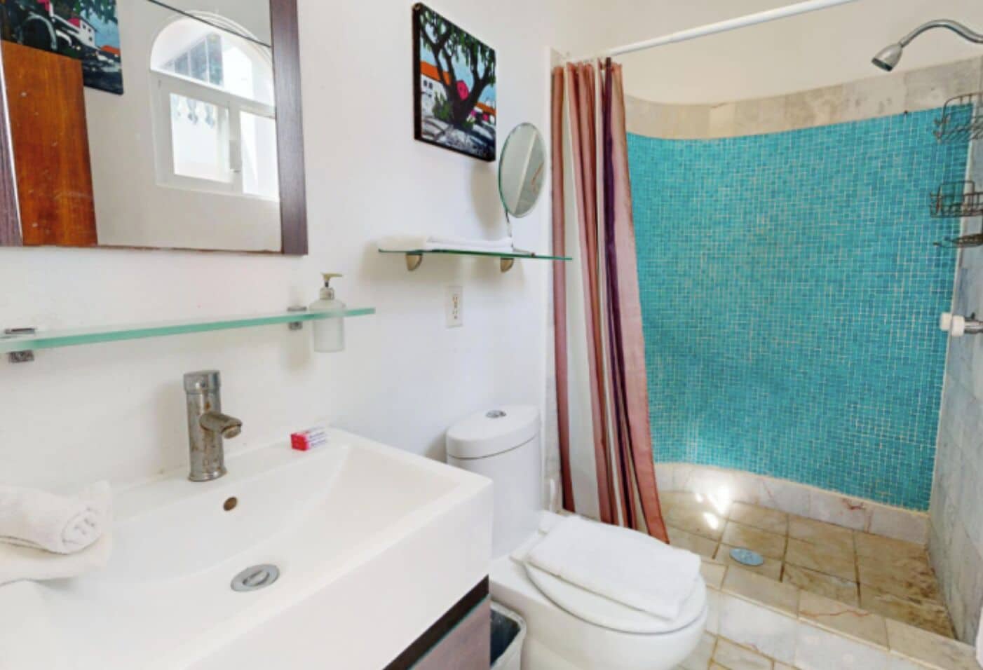 A bathroom with a white sink, a mirror, a toilet, and a shower area with a tiled wall.