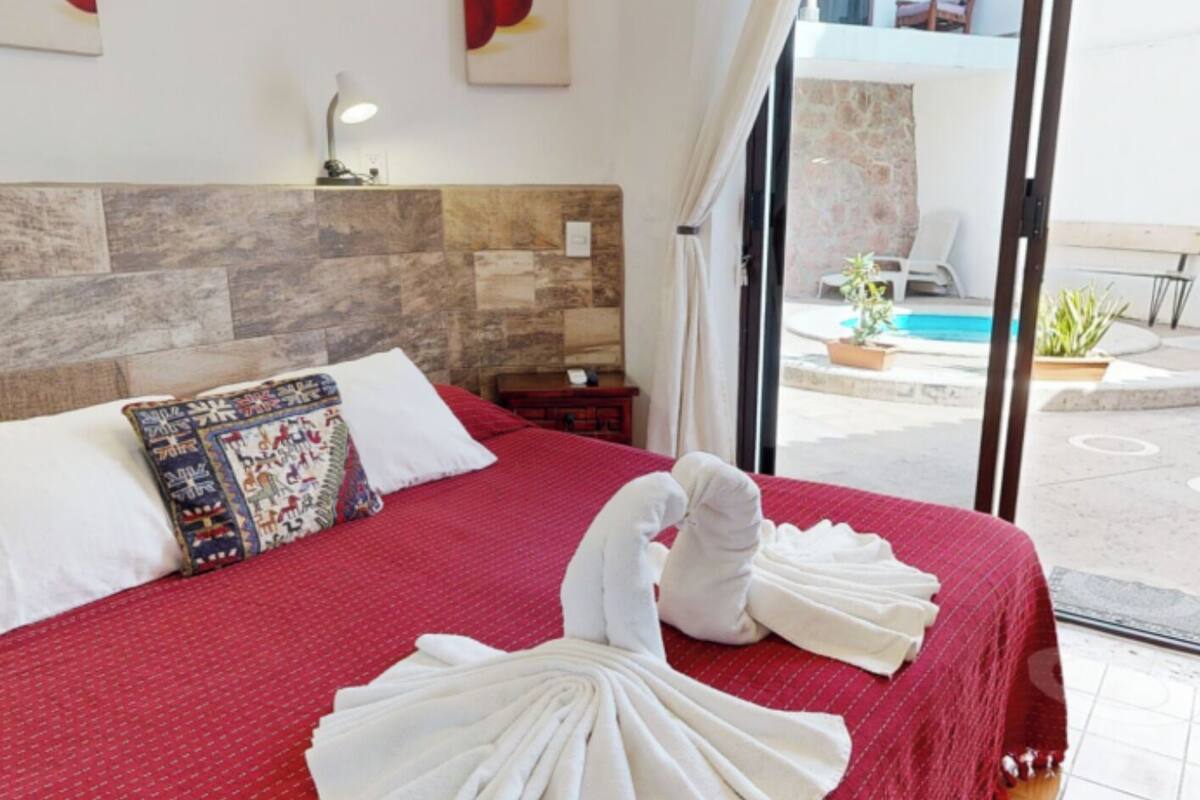 A hotel room with a red bedspread, white pillows, and a view of the pool outside.
