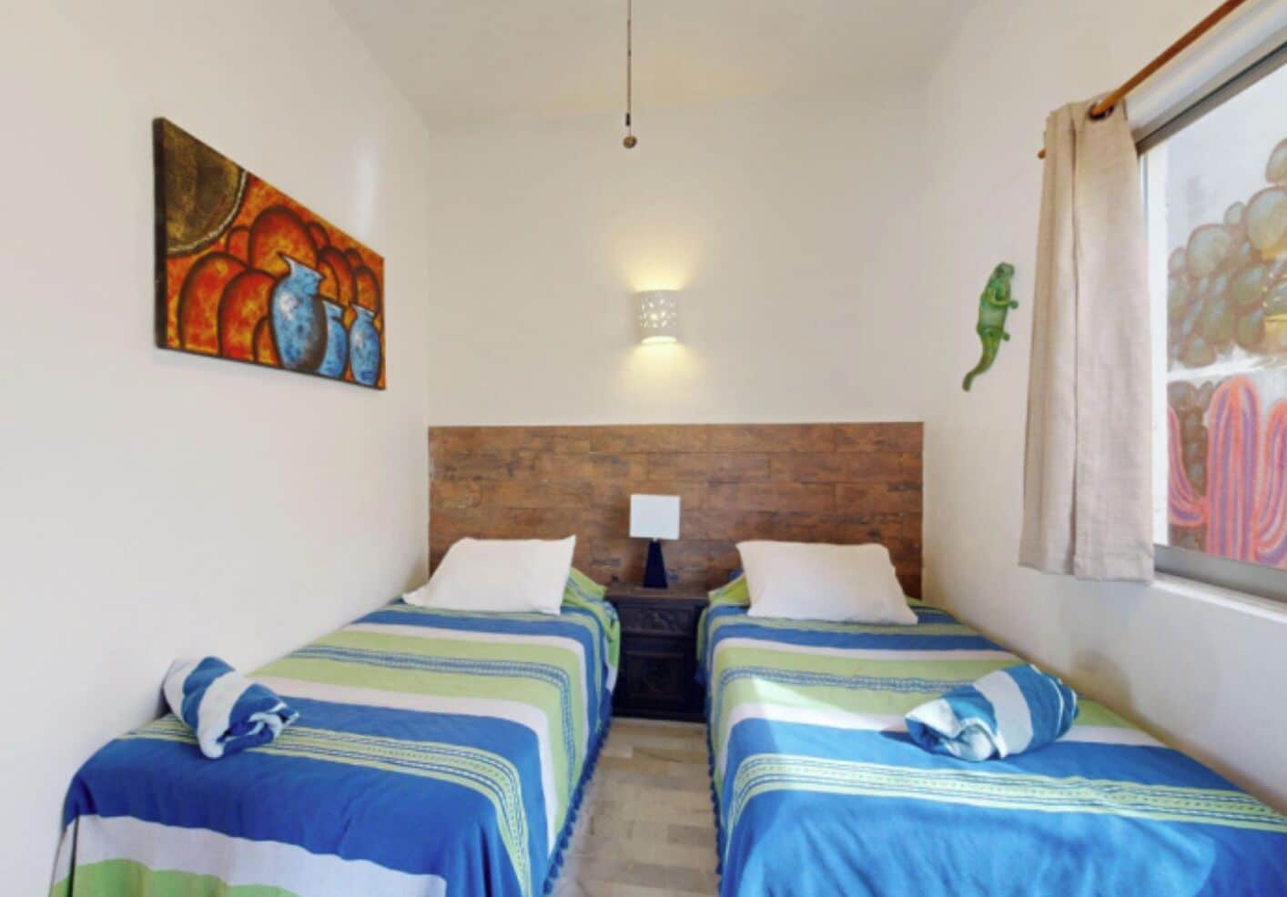 A room with two beds, each with striped bedding, a wooden headboard, a nightstand with a lamp, and a painting on the wall.
