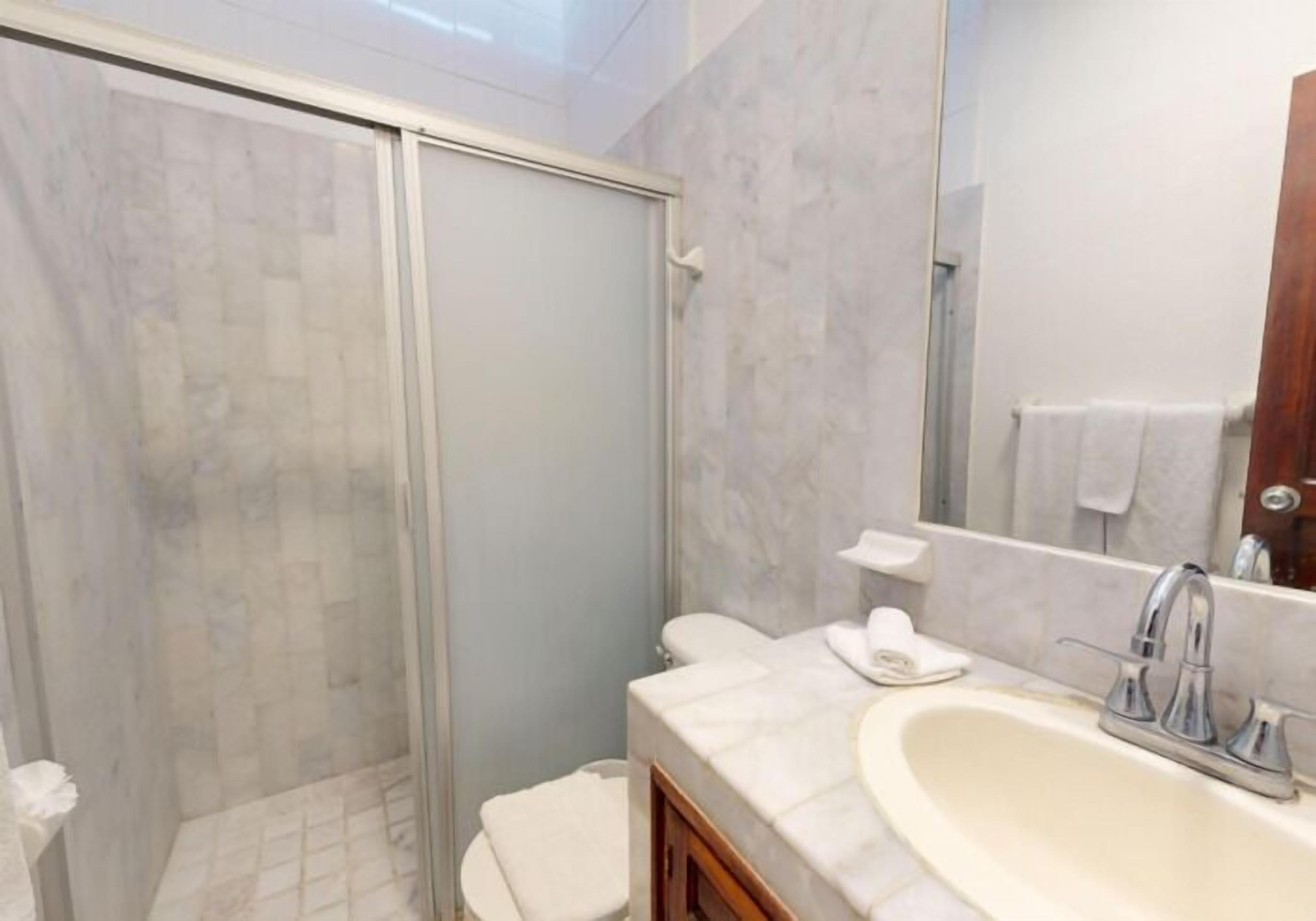 A bathroom with a shower, toilet, sink, and mirror.
