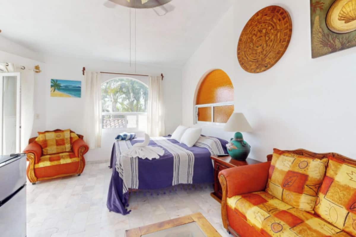 A room with a bed, two sofas, a window, and a ceiling fan.