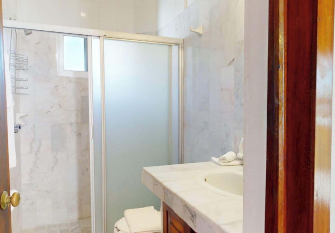 A bathroom with a glass shower enclosure, a white sink, and a marble-tiled wall.