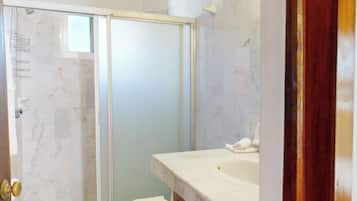 A bathroom with a glass shower enclosure, a white sink, and a marble-tiled wall.