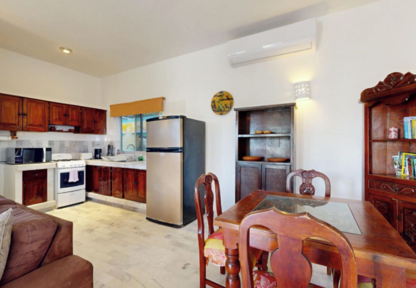 A compact kitchen with wooden cabinets, a refrigerator, and a dining area with a wooden table and chairs.