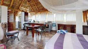 A spacious room with a thatched roof, a dining area with chairs and a table, a bed with a striped blanket, and a kitchenette with a stove and sink. - Aventura Pacifico Boutique Suites Villas (Bucerías)