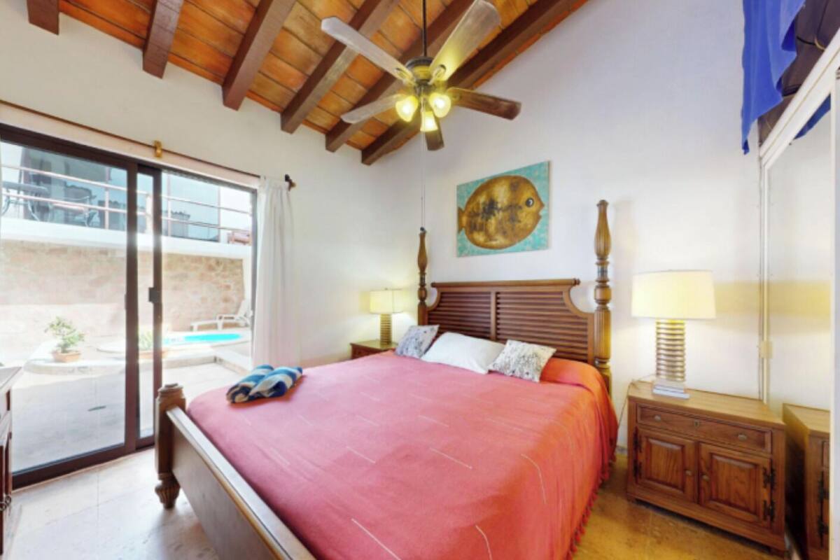 A bedroom with a bed, a ceiling fan, a painting, and a nightstand.