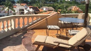 A rooftop terrace with a table and two lounge chairs, overlooking a coastal cityscape with palm trees and buildings. - Aventura Pacifico Boutique Suites Villas (Bucerías)