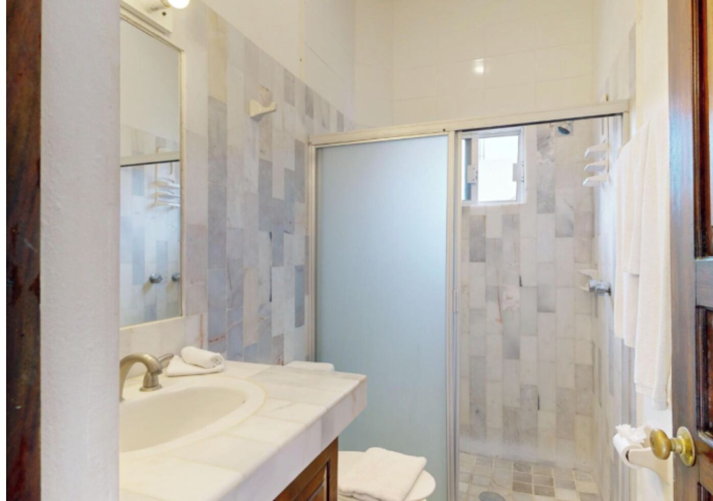 Une salle de bain dotée d’un grand miroir, de deux lavabos, d’une douche avec une porte en verre et d’un porte-serviettes.