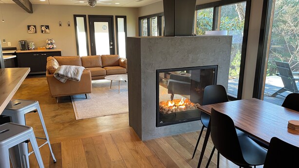 Una sala de estar moderna con chimenea, piso de madera, un sofá y una zona de comedor con sillas y una mesa.