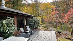 Una terraza de madera con sillas Adirondack, una chimenea de piedra y vistas del follaje otoñal.