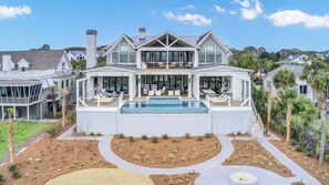 A modern two-story house with a large front deck, a swimming pool, and a well-maintained garden.