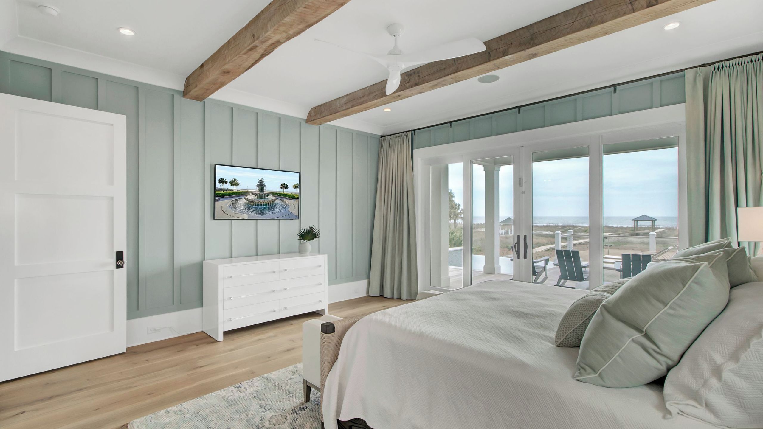 Un dormitorio con cama, cómoda, televisor y vista a la playa.