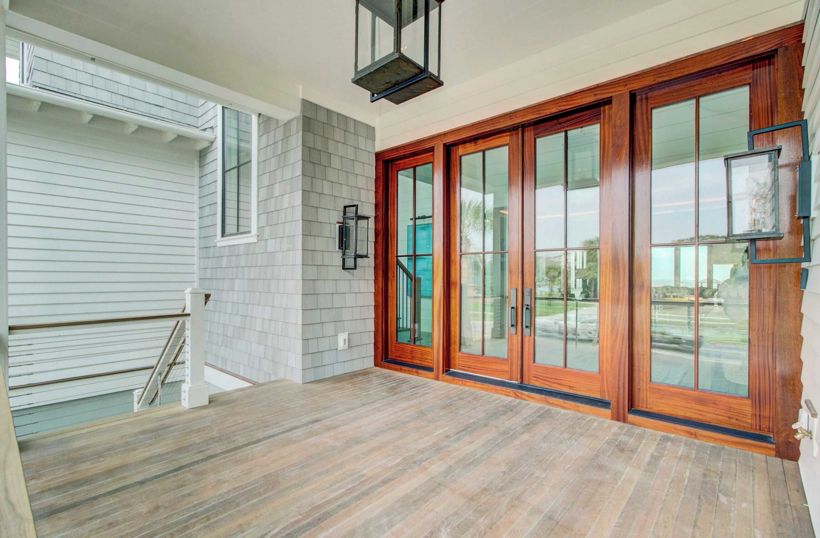 A spacious entryway with a wooden floor, a set of glass doors, and a white exterior wall.