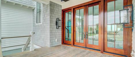 A spacious entryway with a wooden floor, a set of glass doors, and a white exterior wall.