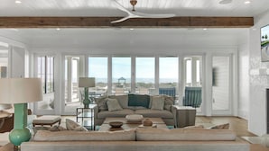 A spacious living room with a large sofa, a coffee table, and a view of the ocean through large windows.