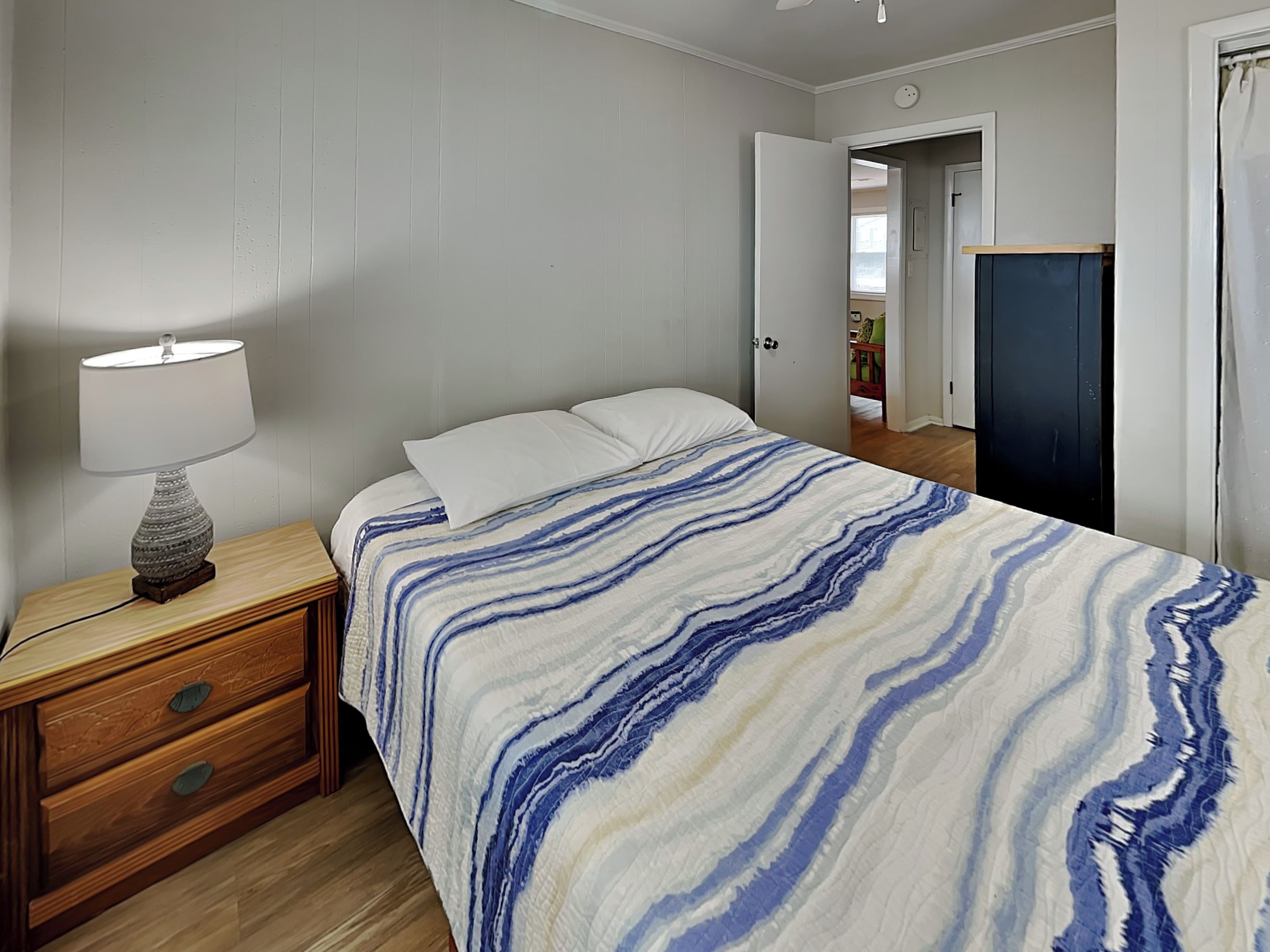 A bedroom with a bed, a nightstand, a lamp, and a door leading to another room.
