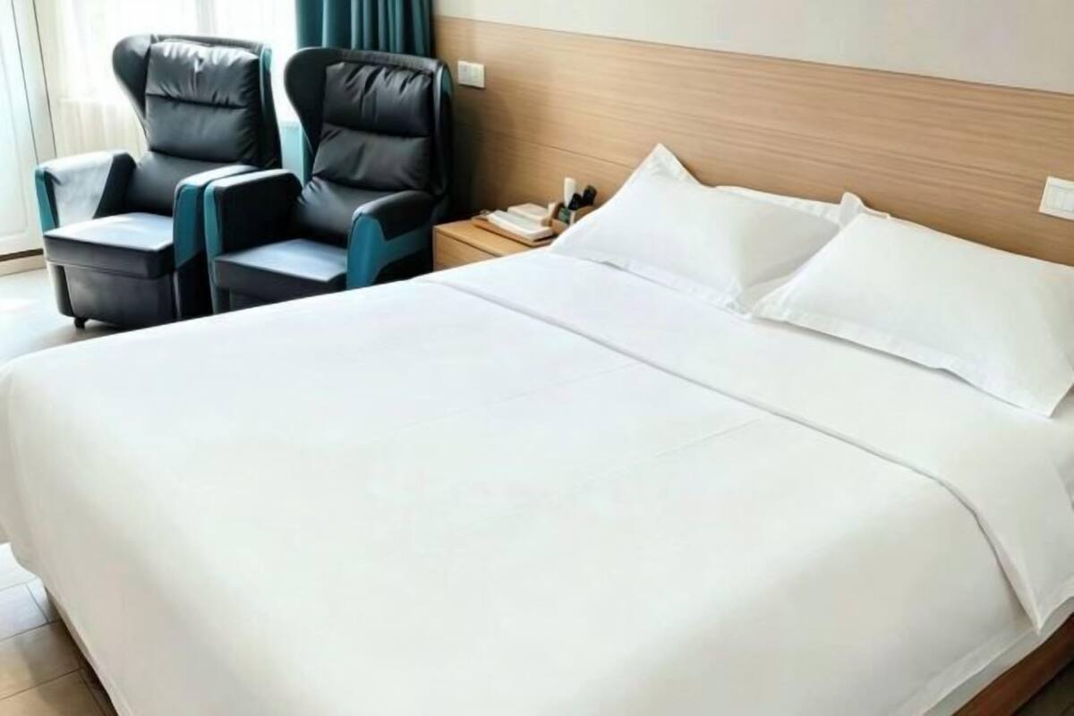 Habitación de hotel con una cama grande, dos sillones de cuero negro, un cabecero de madera y una mesita de noche con un libro y un teléfono.