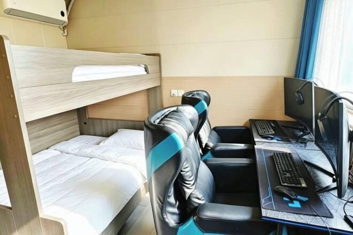 Una cama litera con escritorio y equipo de computadora, una ventana con cortinas y un respiradero en la pared.