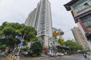 Un edificio residencial alto con diseño moderno, rodeado de árboles y otros edificios.