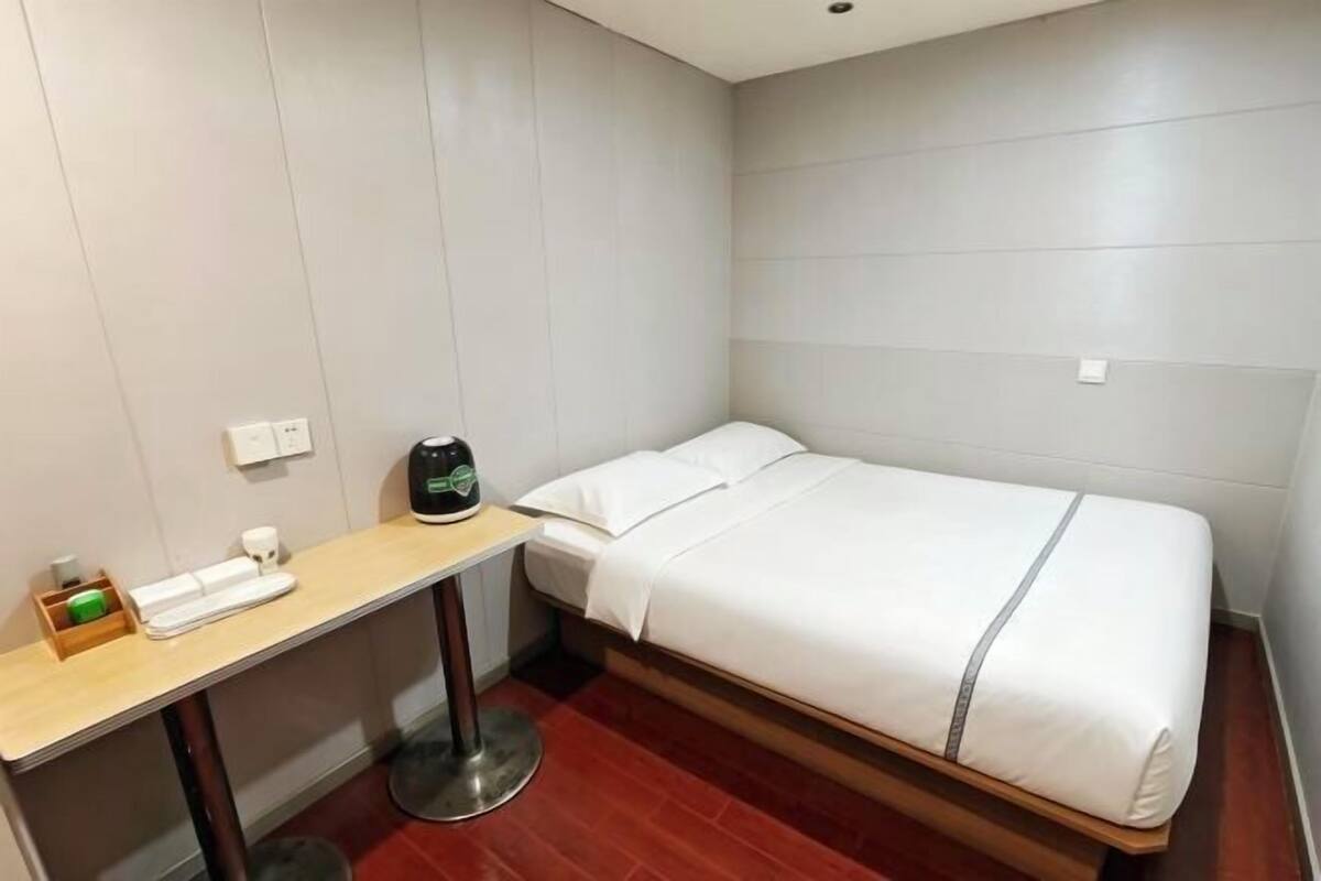 Una habitación de hotel pequeña con una cama individual, un escritorio, una silla y una tetera.