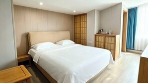 Une chambre d’hôtel avec un grand lit, une tête de lit en bois, une petite table de chevet en bois, une armoire en bois et une vue sur l’extérieur par une fenêtre avec des rideaux.