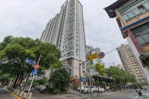 Un edificio residencial alto con varios pisos, rodeado de árboles y automóviles estacionados.