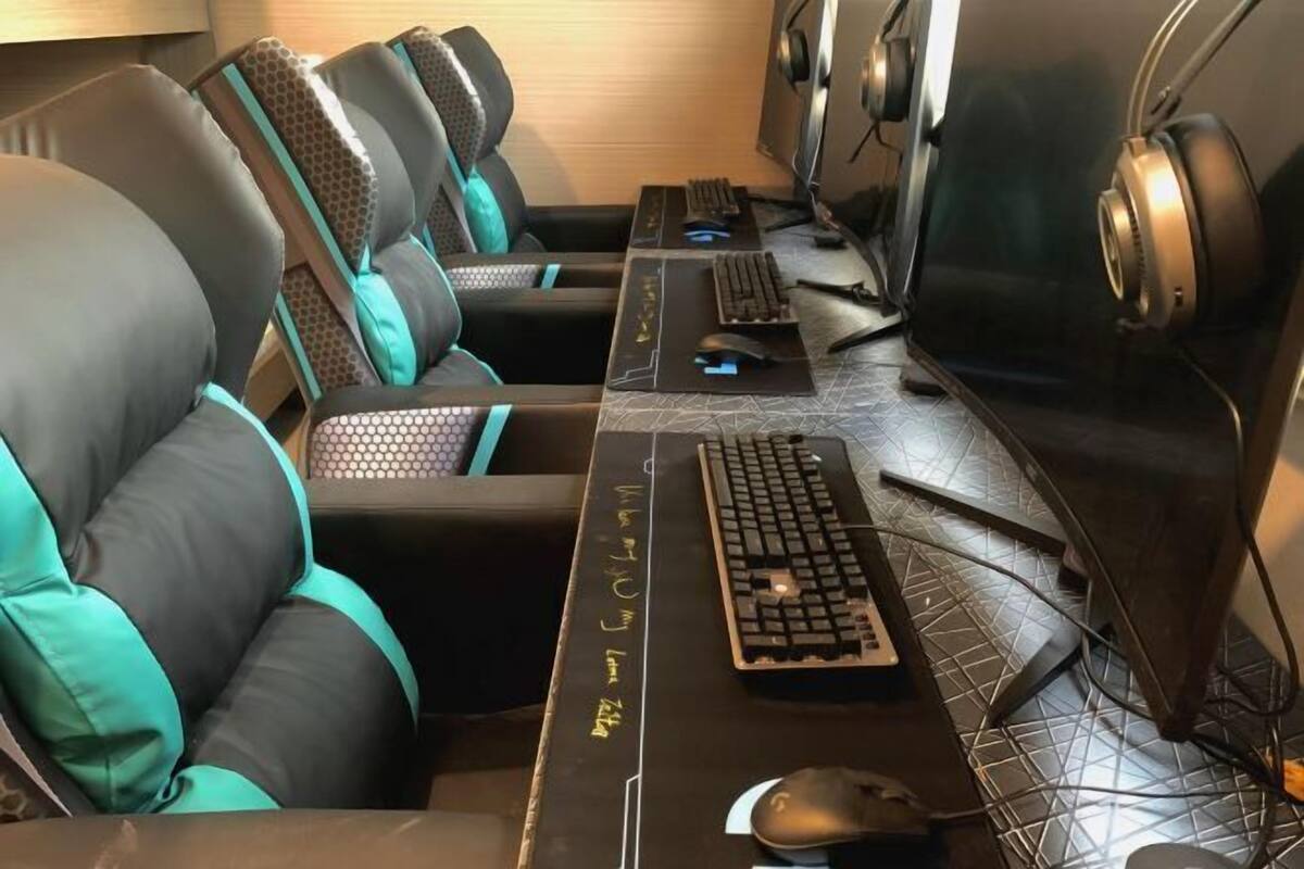 Una configuración para videojuegos con varias sillas, un escritorio con teclado, ratón y auriculares, y dos monitores.