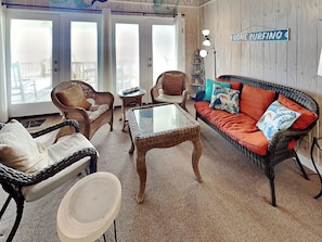 A cozy living room with wicker furniture, a glass-top coffee table, and a red sofa with tropical pillows.