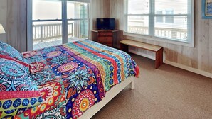 A bedroom with a large bed, a ceiling fan, a TV, and a balcony. - Blue Shamu by Topsail Realty (Holly Ridge)