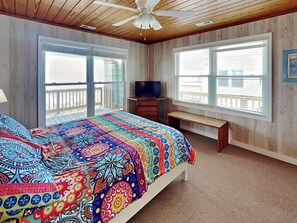 A bedroom with a large bed, a ceiling fan, a TV, and a balcony. - Blue Shamu by Topsail Realty (Holly Ridge)