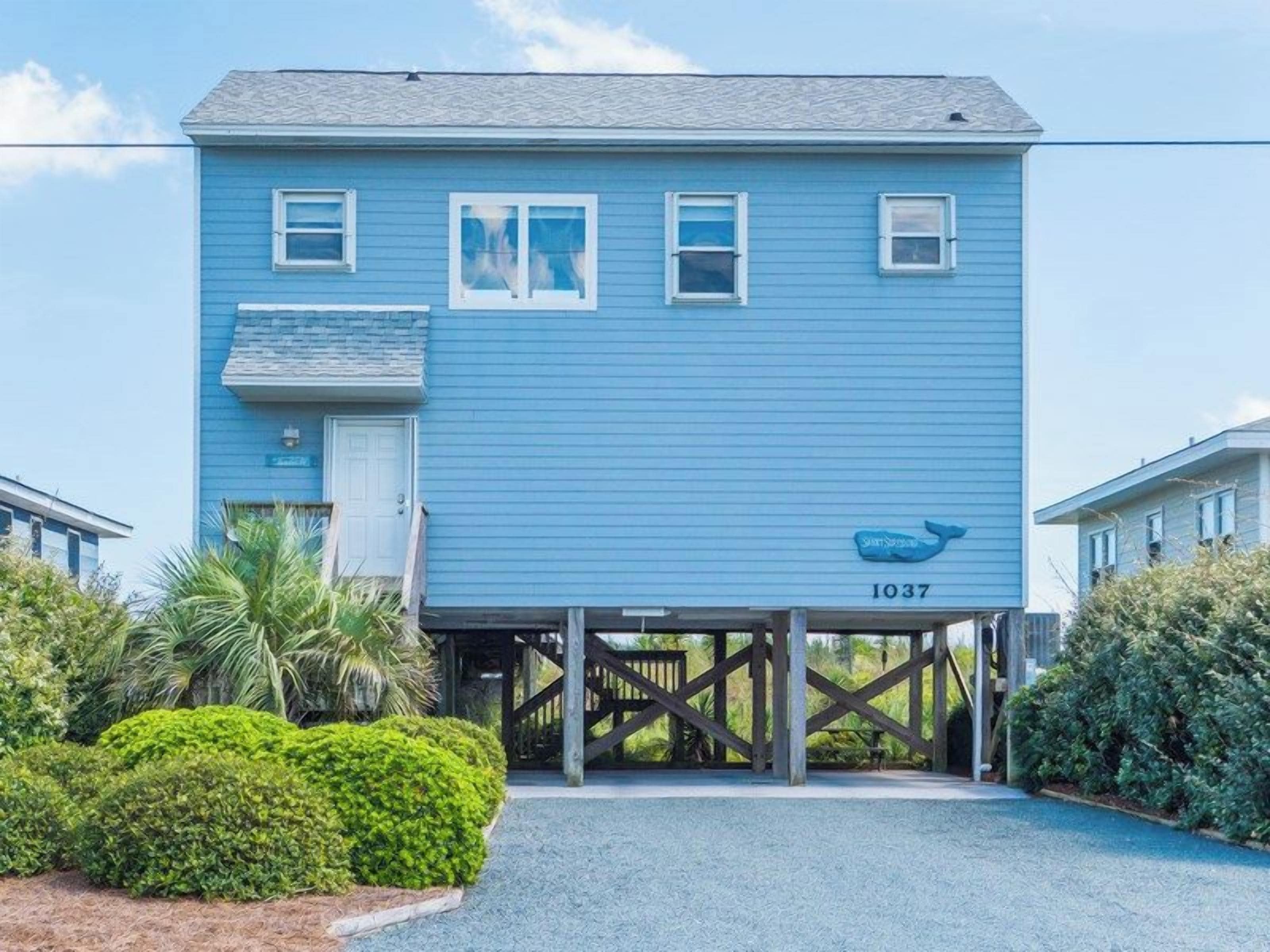 A two-story building with a blue exterior, numbered 1037, featuring a small balcony and a wooden deck.