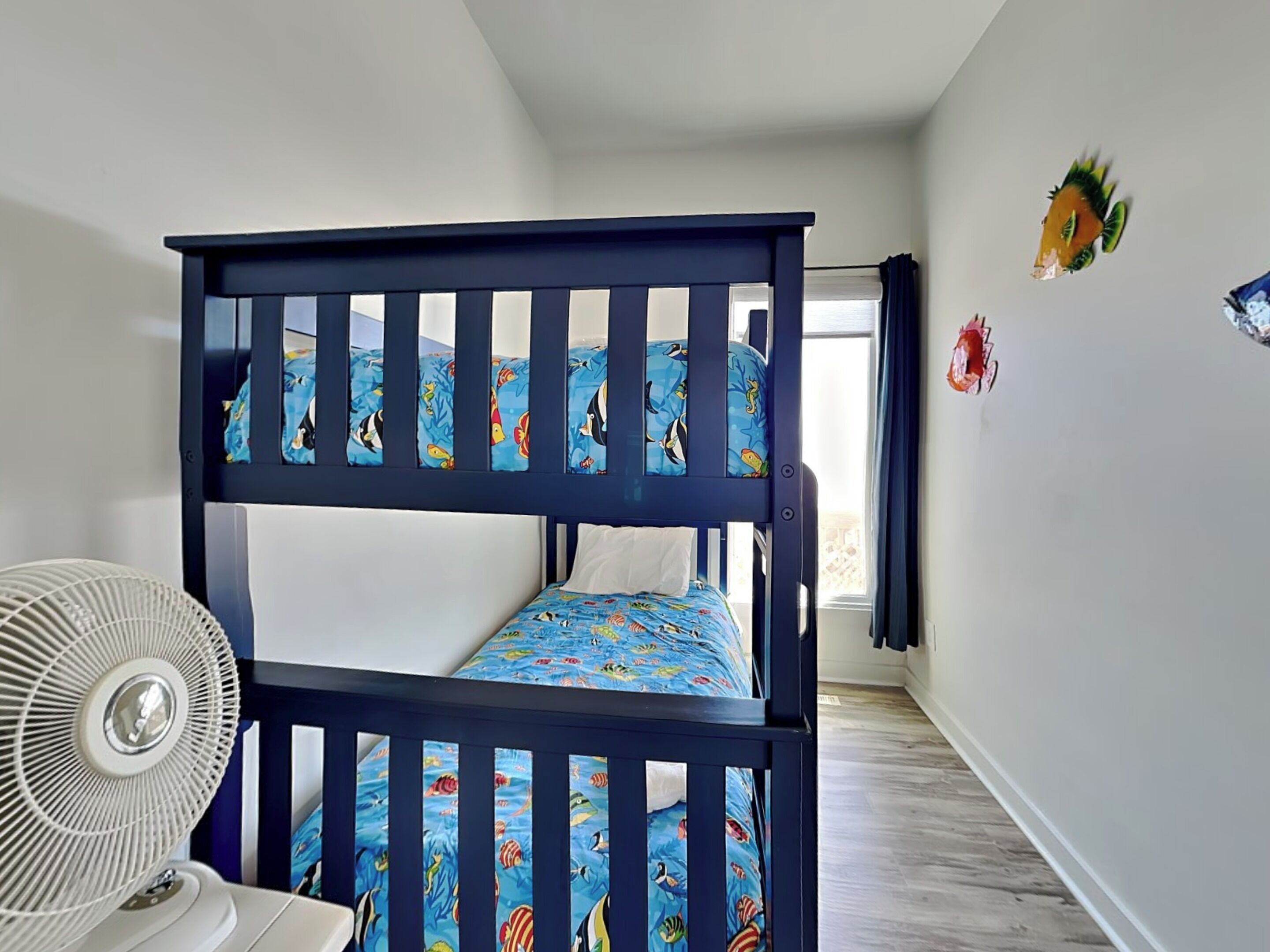 A bunk bed with a fan, a window, and a wall with a fish decoration.