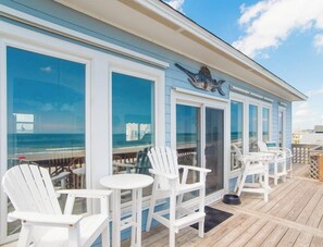 A deck with white chairs and tables, overlooking the ocean. - Sweet Surrender by Topsail Realty (Holly Ridge)
