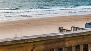 Una playa con una baranda de madera al frente, una orilla arenosa y el océano al fondo.