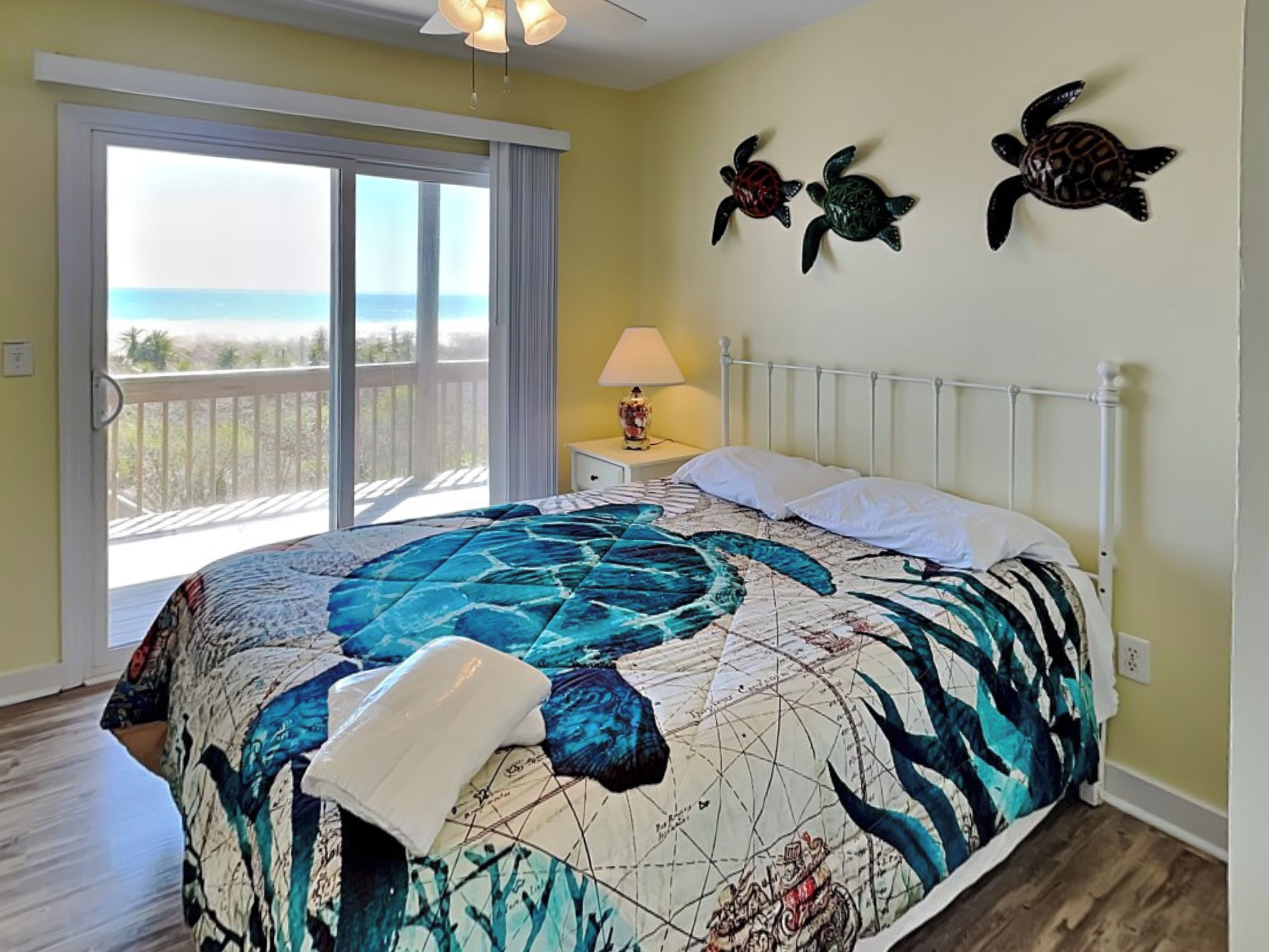 A bedroom with a large bed, a sliding glass door to the balcony, and three turtle wall art pieces.