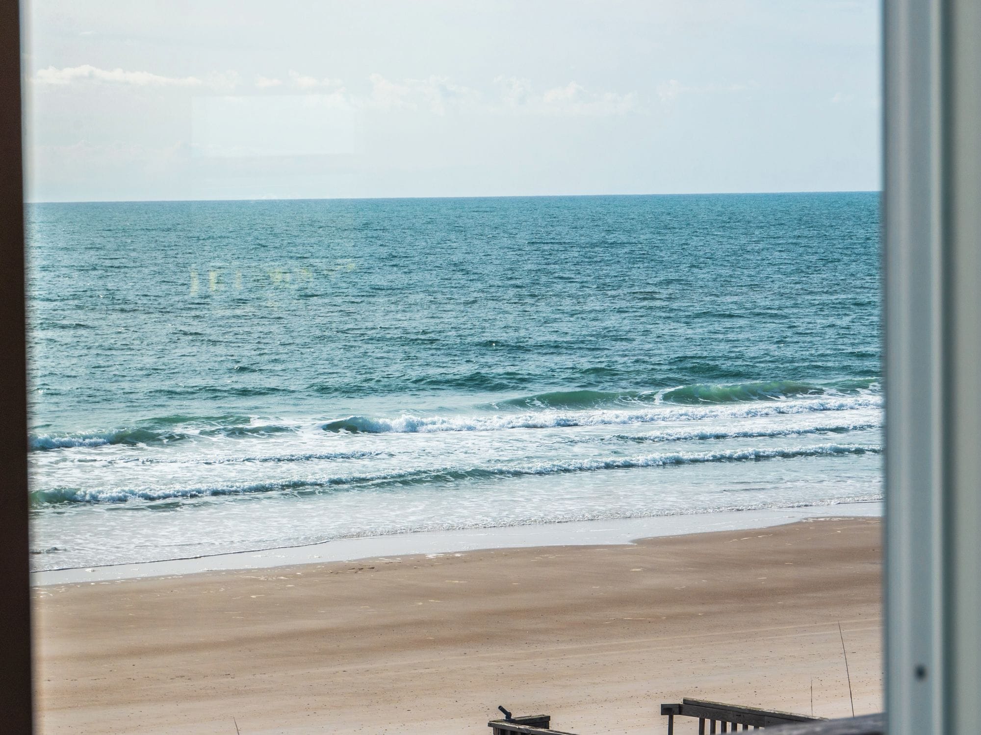 A beach view with a wooden fence and a clear sky.