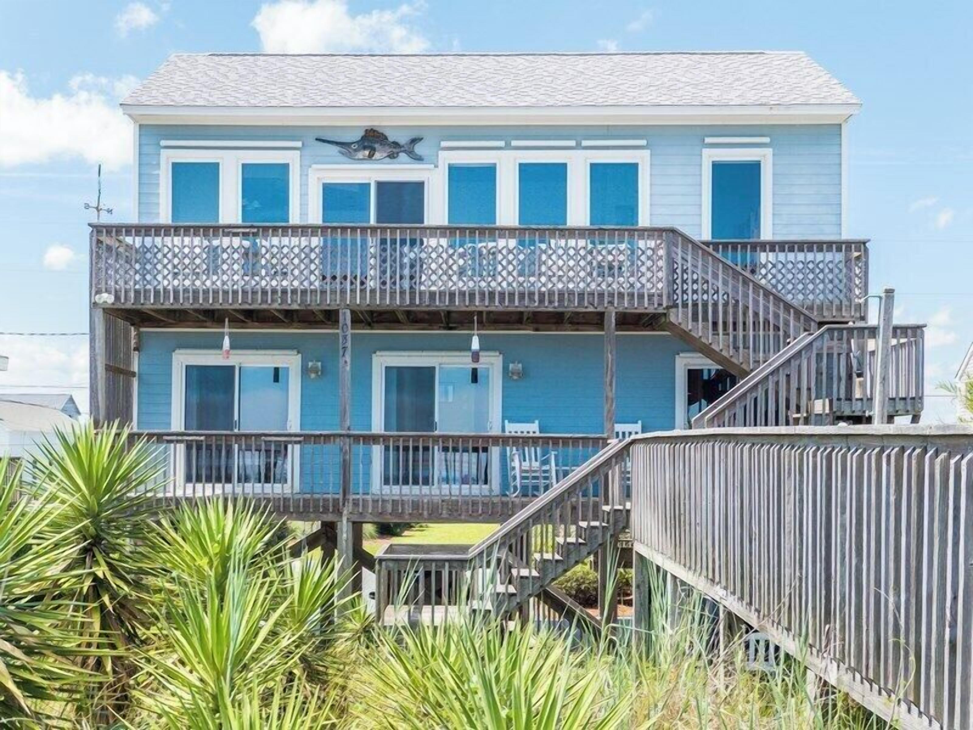Una casa frente al mar de dos pisos con un balcón y una escalera que conduce al nivel superior.