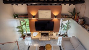 A modern living room with a flat-screen TV, wooden beams, bookshelves, and potted plants. - Altiora - Luxury loft in Rome (Roma)