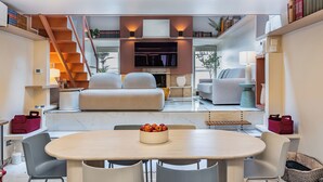 A modern living room with a dining area, a staircase, and a flat-screen TV mounted above a fireplace. - Altiora - Luxury loft in Rome (Roma)