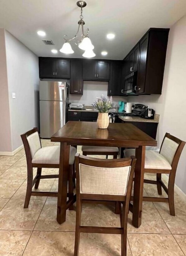 A modern kitchen with dark cabinets, a stainless steel refrigerator, a built-in oven, and a coffee maker on the counter. - Lavender home: King & Queen (Edinburg)