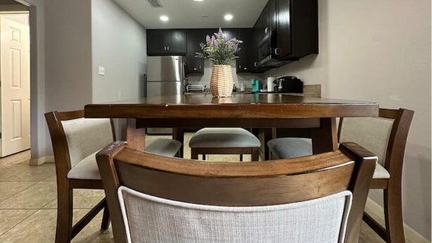 Un coin repas avec une table et des chaises en bois, un lustre et une cuisine en arrière-plan.