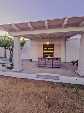 A covered outdoor seating area with a table and chairs, surrounded by concrete pillars and potted plants. - Da Riccardo (Carloforte)